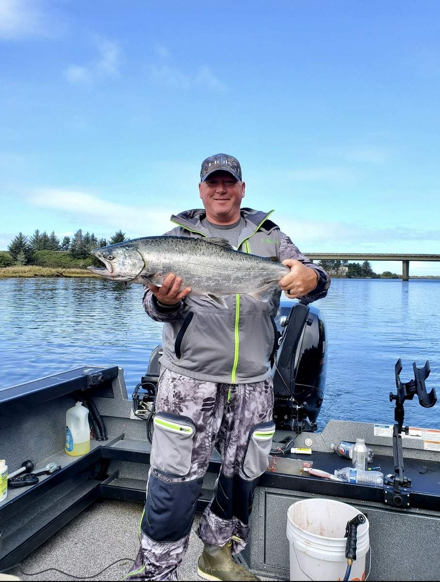 Angler holding a chrome Chinook salmon on a bluebird day near Lincoln City